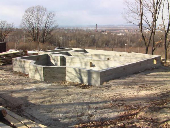 Fundamenty domu jednorodzinnego z betonu na etapie budowy, widok z góry na tle krajobrazu miejskiego w oddali.