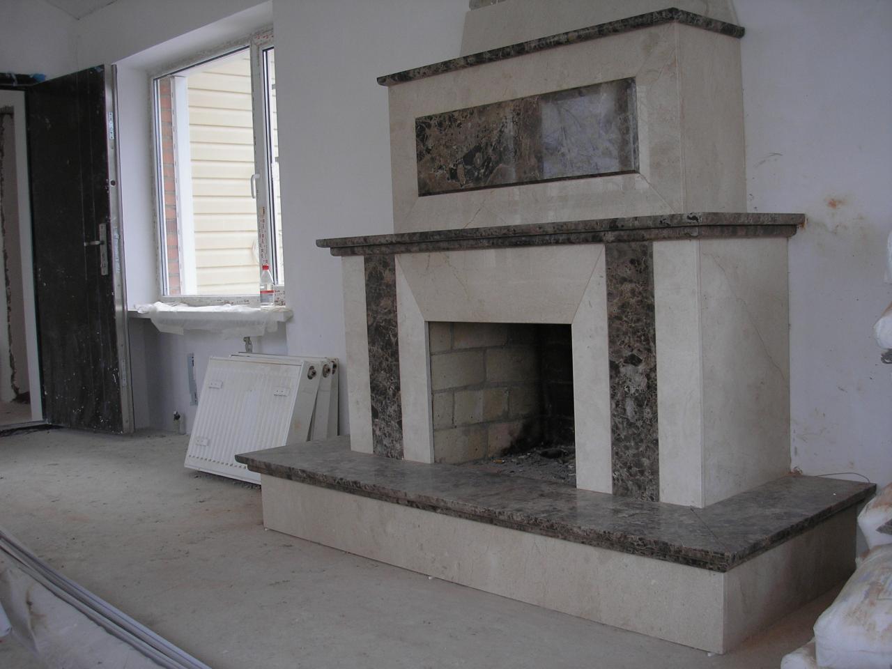 Marmurowy kominek w trakcie montażu, widoczne niedokończone wykończenia wnętrza i grzejnik oparty o ścianę.