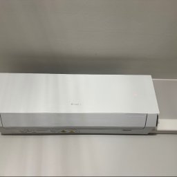 Climca-M Kamil Żabik - Biała jednostka klimatyzacyjna GREE zamontowana na jasnoszarej ścianie, z widocznym czerwonym wskaźnikiem i białym korytem instalacyjnym po prawej.