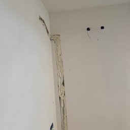 Climca-M Kamil Żabik - Wykute w białych ścianach kanały z rurami i pianką izolacyjną, przygotowanie pod instalację w Legionowie. Widoczne otwory na przewody.