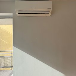Climca-M Kamil Żabik - Biały system chłodzący LG Inverter V na jasnoszarej ścianie, z ukośnym cieniem i fragmentem balkonu z żółtą elewacją.