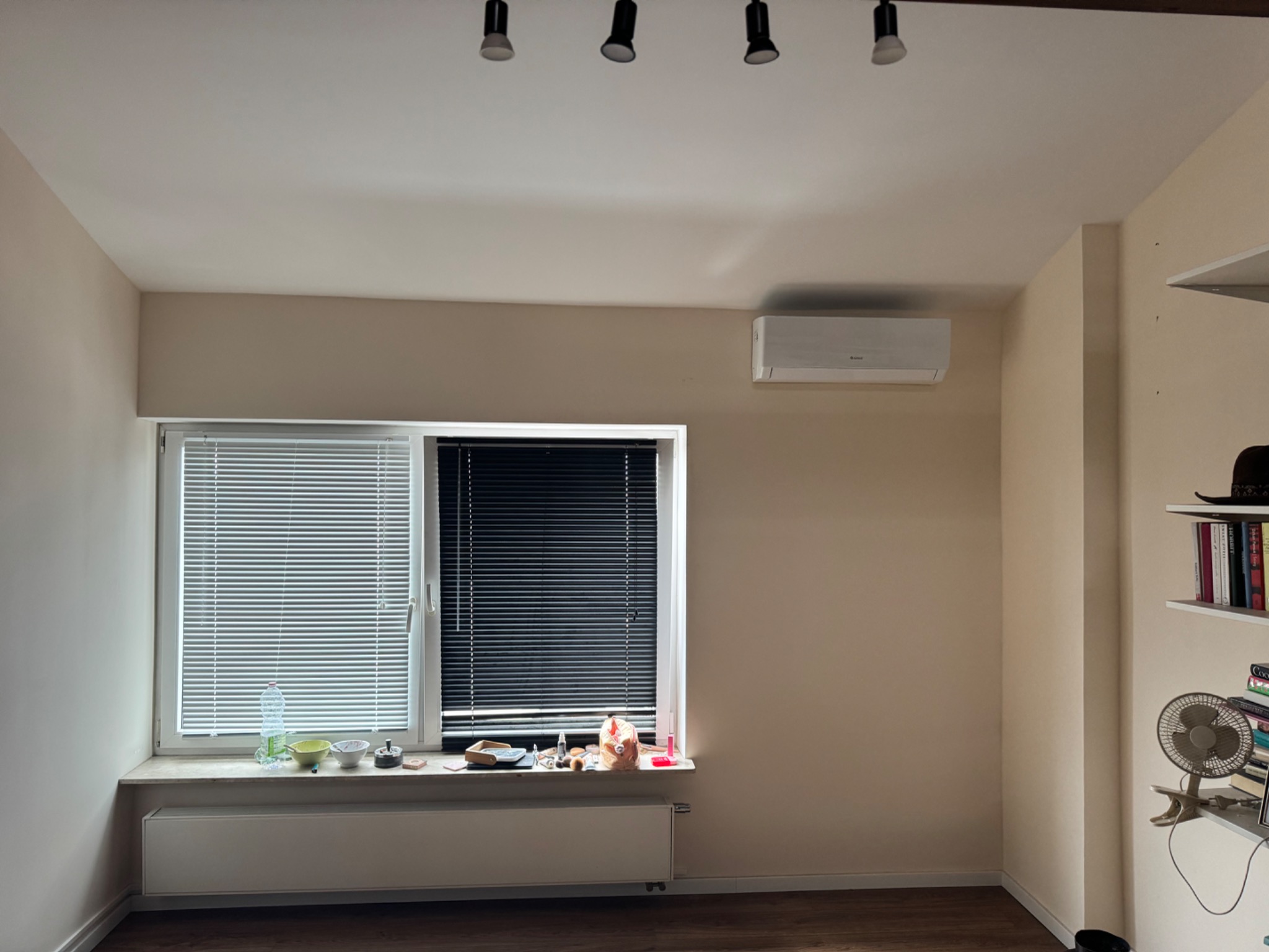 Zainstalowana biała klimatyzacja ścienna w jasnym, minimalistycznym pokoju z beżowymi ścianami, oknem z żaluzjami i drewnianą podłogą.