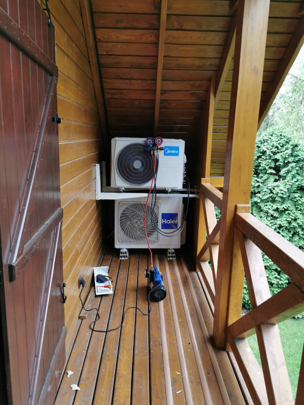 Dwa agregaty klimatyzacyjne (Midea i Haier) zamontowane na drewnianym balkonie podczas serwisu, widoczne narzędzia i przewody serwisowe.