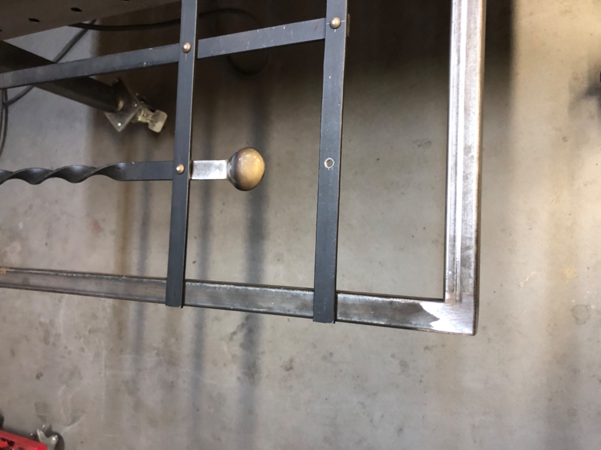 Metalowa konstrukcja z prętami i ozdobnym uchwytem z kulką, widoczne ślady po obróbce na surowym betonie.