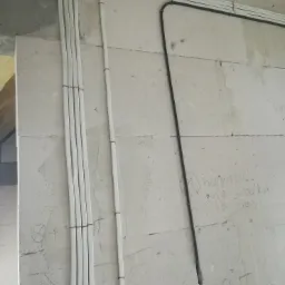 Białe i czarne przewody elektryczne prowadzone po szarej ścianie z betonu komórkowego, zabezpieczone czarnymi opaskami zaciskowymi.