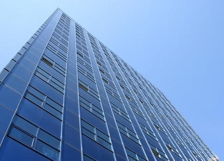 Wysoki, nowoczesny budynek biurowy z niebieską szklaną fasadą sfotografowany pod ostrym kątem z dołu w Łodzi, na tle błękitnego nieba.