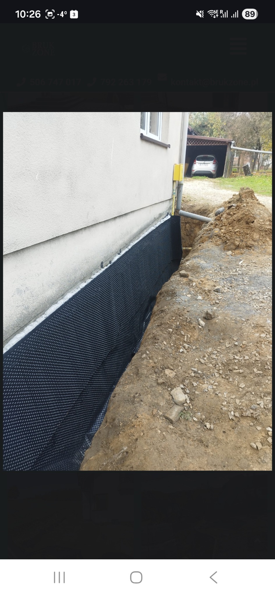 Ochrona fundamentów budynku z użyciem folii kubełkowej, widoczny wykop i fragment ściany. Prace ziemne w toku, zarys domu w tle.