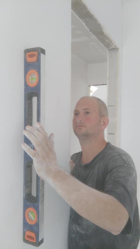 Pracownik w Poznaniu sprawdza pion ściany przy użyciu poziomicy w trakcie prac wykończeniowych w nowo wykończonym pomieszczeniu.