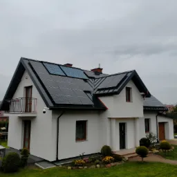 Nowoczesny dom jednorodzinny z białą elewacją i panelami słonecznymi na dachu w pochmurny dzień, widok z poziomu gruntu