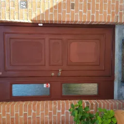 Odnowione, ciemnobrązowe, drewniane drzwi wejściowe z szybami, osadzone w ceglanej wnęce z numerem domu '74'.