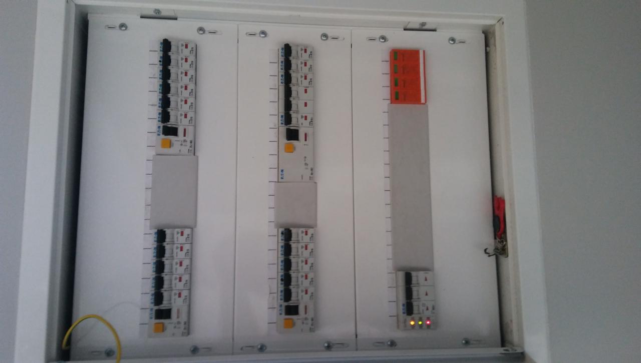 Rozdzielnica elektryczna w białej obudowie z widocznymi bezpiecznikami, listwami zaciskowymi i przewodami, z trzema diodami sygnalizacyjnymi świecącymi na dole po prawej stronie.