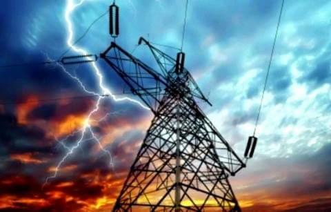 Słup wysokiego napięcia z widocznym wyładowaniem atmosferycznym na tle dramatycznego, wielobarwnego nieba.