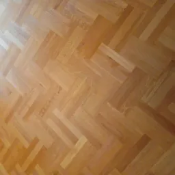 Parkiet ułożony w jodełkę z jasnego drewna, widoczne naturalne usłojenie i delikatny połysk, oświetlenie z lewej strony tworzy subtelny gradient.