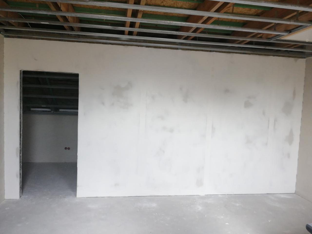 Ściana po szpachlowaniu łączeń płyt, widoczne metalowe profile sufitowe, przygotowanie do dalszych prac wykończeniowych.