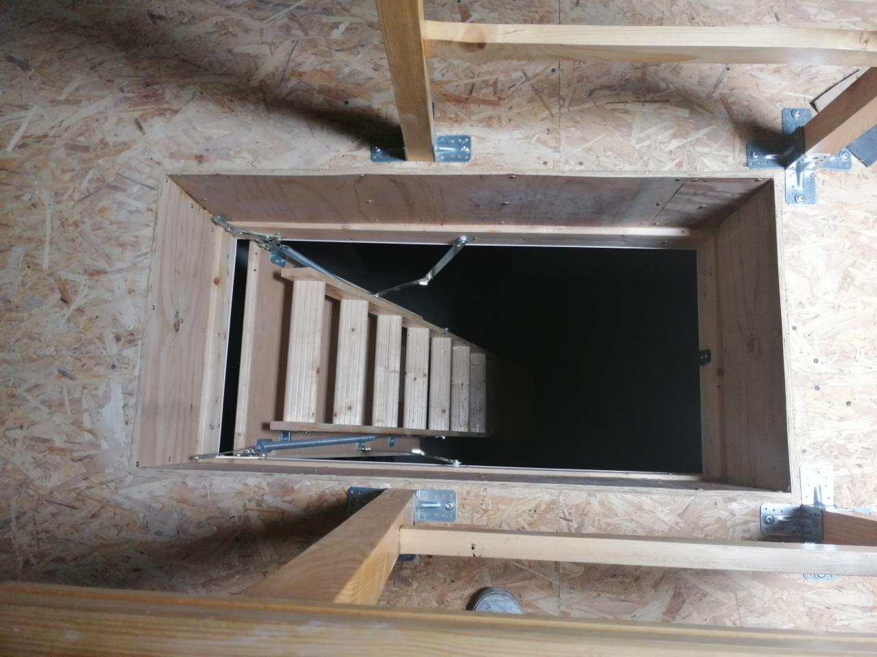 Otwór w stropie z zamontowanymi składanymi schodami strychowymi, widoczne elementy konstrukcyjne z drewna i płyty OSB.