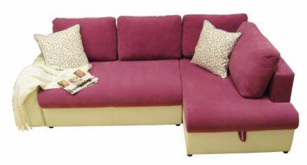 Różowa, narożna sofa z beżową podstawą, ozdobiona wzorzystą poduszką i kremowym pledem z frędzlami, na której leży magazyn.