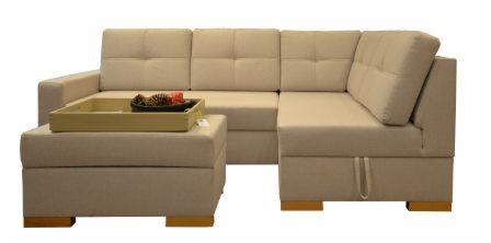 Jasnobeżowy, modułowy narożnik z pufem i drewnianymi nóżkami, na pufie taca z dekoracjami.