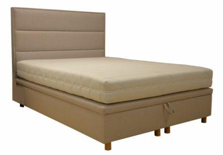 Tapicerowane łóżko kontynentalne w odcieniach beżu, z wezgłowiem w poziome pasy i materacem na skrzyni z szufladami, widoczne nóżki z jasnego drewna.