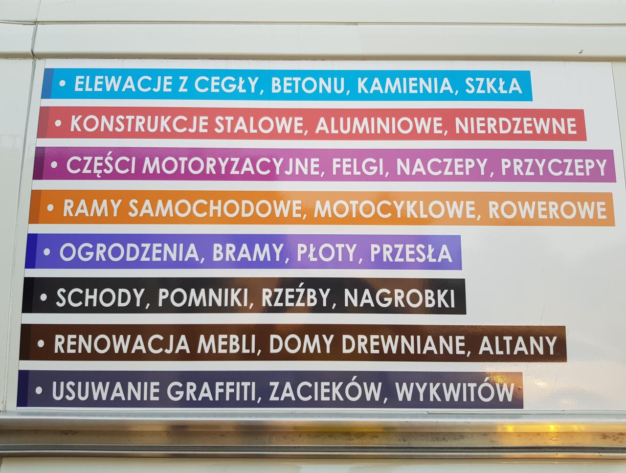 Tablica reklamowa z wypisanymi usługami: elewacje, konstrukcje stalowe, części motoryzacyjne, ramy, ogrodzenia, schody, renowacja mebli, usuwanie graffiti.