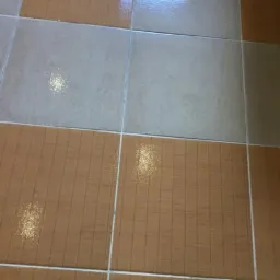 Błyszcząca podłoga z płytek w odcieniach beżu i brązu, widoczne odbicia światła po umyciu.