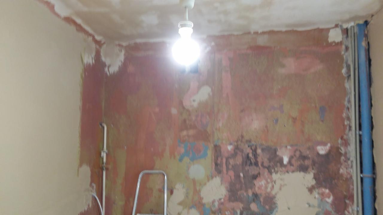 Pokój w trakcie przygotowania do malowania, z widocznymi śladami starej farby, częściowo otynkowanymi ścianami i drabinką w rogu.