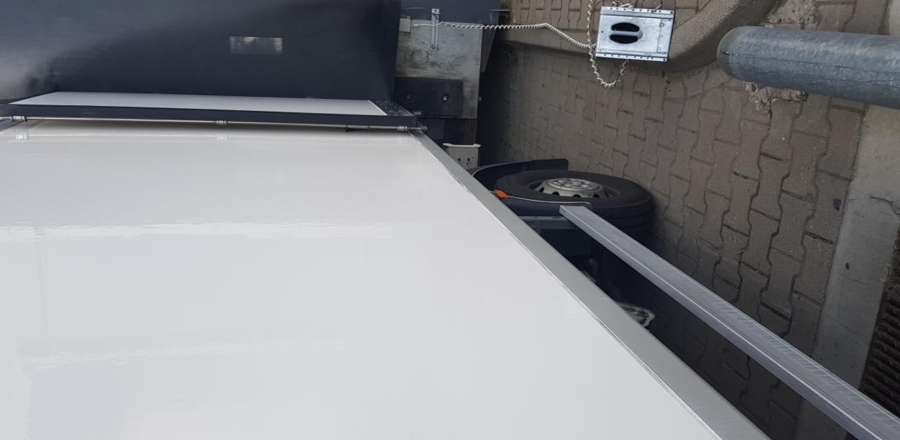 Biała plandeka naczepy ciężarowej widziana z góry, z widocznym kołem zapasowym i elementami konstrukcyjnymi pojazdu.