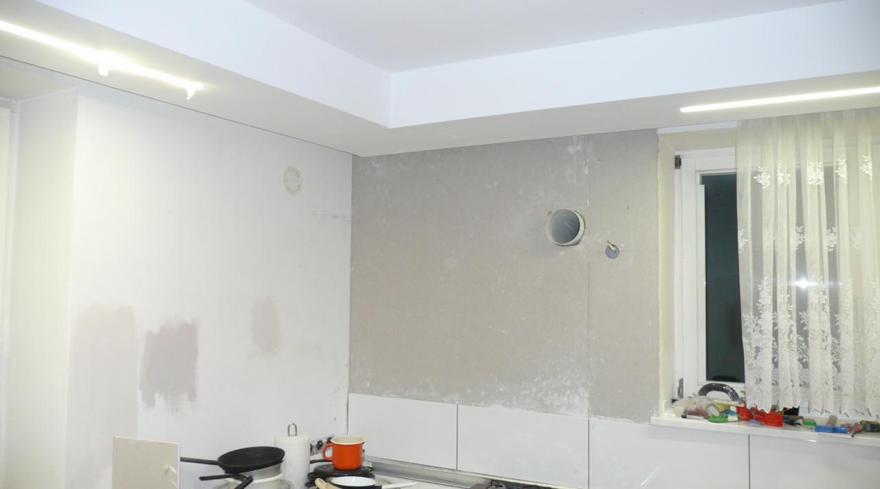 Wnętrze kuchni w trakcie remontu, widoczne przygotowane ściany pod zabudowę, otwór wentylacyjny, okno z firanką i akcesoria kuchenne na blacie.