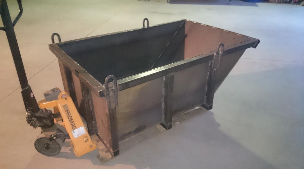 Surowy, spawany kontener transportowy z uchwytami, umieszczony na żółtym wózku paletowym marki Promag na gładkiej, betonowej posadzce.