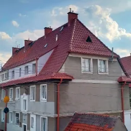 Wielorodzinny budynek z czerwoną dachówką, widok z góry, z trójkątnym oknem dachowym i satelitami na elewacji.