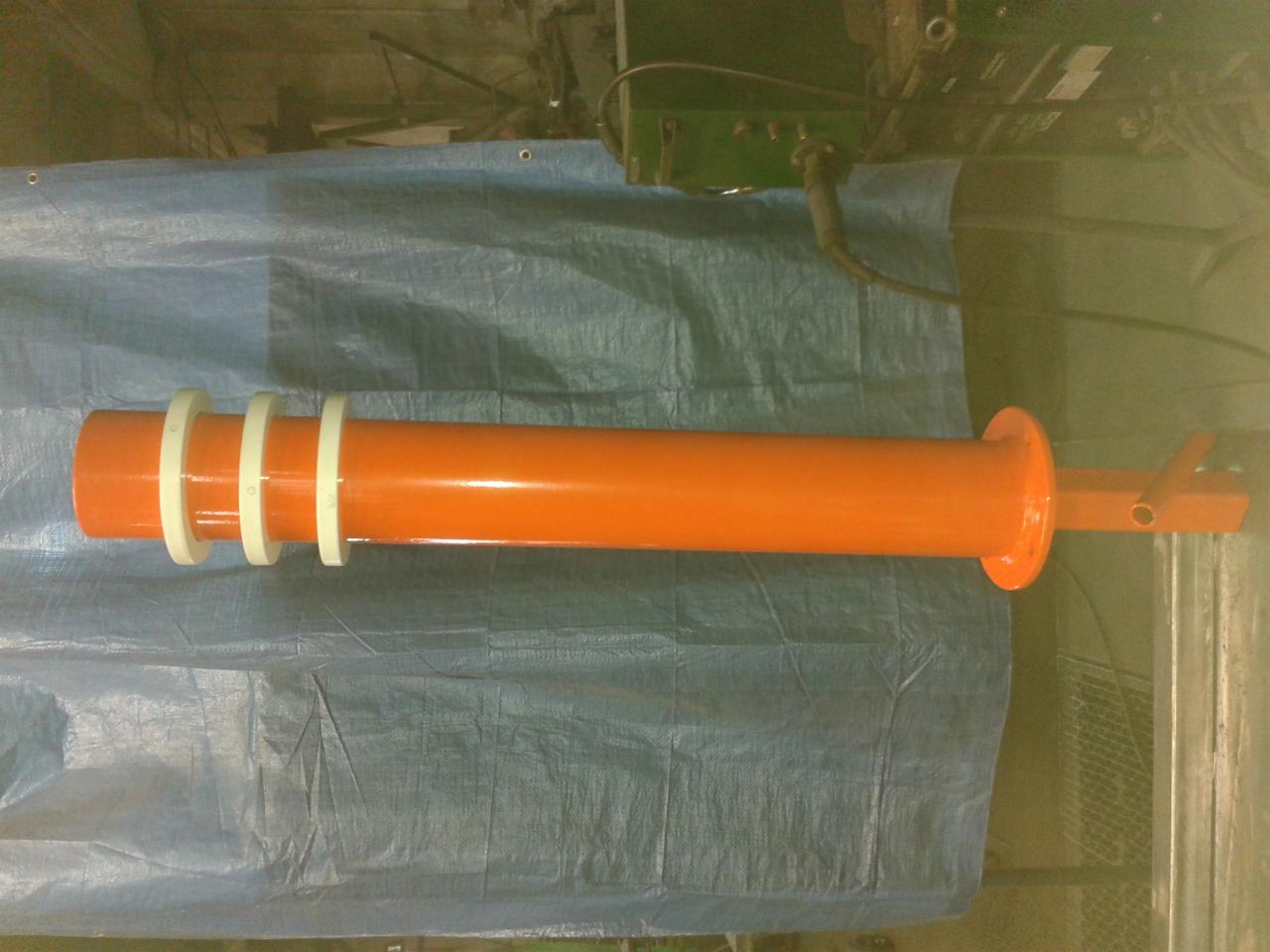 Pomarańczowy, pomalowany proszkowo element konstrukcyjny z trzema białymi pierścieniami na niebieskiej plandece w hali.