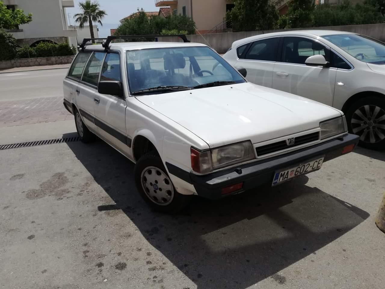 Białe kombi z bagażnikiem dachowym zaparkowane na chodniku w słoneczny dzień, widoczny numer rejestracyjny MA 602-CE.