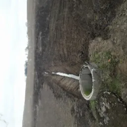 Wykonany wykop pod instalację, z widocznym betonowym kręgiem na skraju, ziemia świeżo przekopana, w oddali widoczne drzewa.