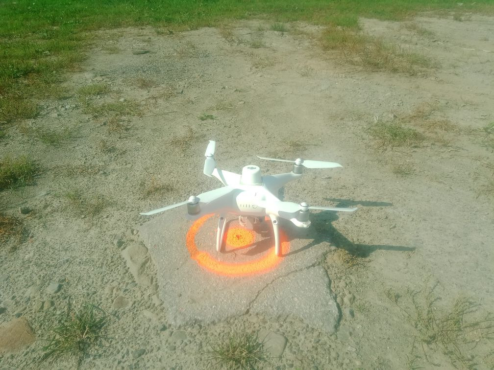 Biały dron na betonowej płycie z pomarańczowym okręgiem, trawa w tle.