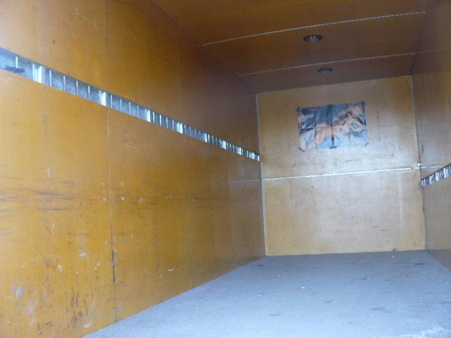 Wnętrze pustej skrzyni ładunkowej pojazdu z żółtymi ścianami i metalowymi listwami mocującymi. Na tylnej ścianie przyklejony plakat.