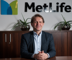 Portret uśmiechniętego mężczyzny w garniturze na tle biura z logo MetLife i roślinami doniczkowymi.