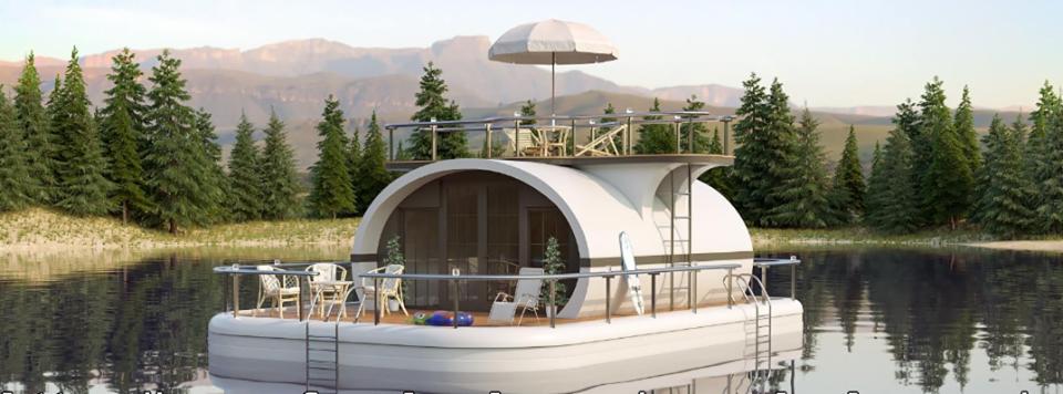 Wizualizacja pływającego, modułowego domu z tarasem na wodzie, otoczonego lasem iglastym i górami w tle.