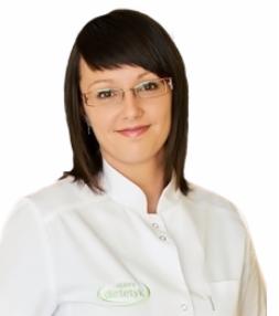 Uśmiechnięta dietetyczka w okularach i białym fartuchu, z identyfikatorem z logo, na jasnym tle. Portret w neutralnym oświetleniu.