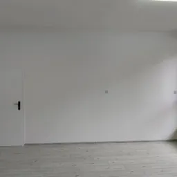 Pusty pokój po remoncie z białymi ścianami, szarą podłogą imitującą drewno i białymi drzwiami z czarną klamką, widok na zieleń przez okno.