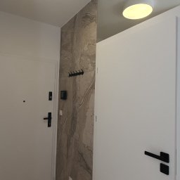 WB-Qube Waldemar Bednarczyk - Nowoczesny przedpokój z białymi drzwiami, płytkami imitującymi kamień na ścianie, okrągłym plafonem i wieszakiem na ubrania.