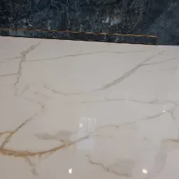 Błyszczące, marmurowe płytki podłogowe w łazience z odpływem liniowym i fragmentem ciemnej ściany imitującej kamień. Widoczny narożnik zabudowy.