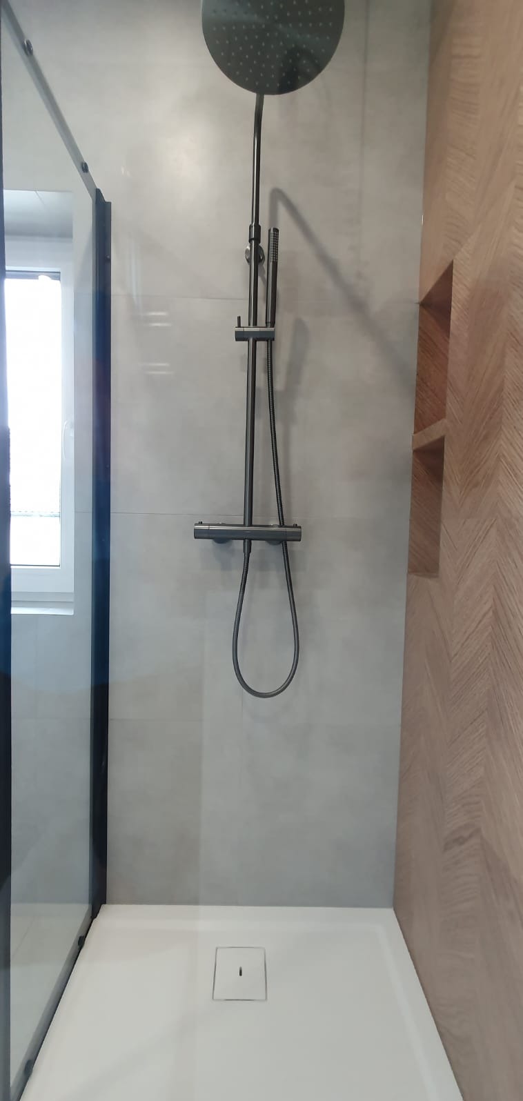 Nowoczesna kabina prysznicowa z deszczownicą i odpływem liniowym, wykończona płytkami w odcieniach szarości i drewnopodobną ścianą z wnękami.