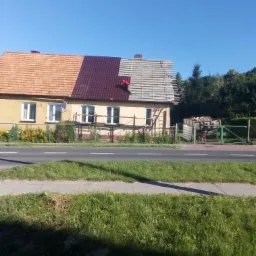 Dom jednorodzinny z częściowo wymienionym pokryciem dachowym; po lewej stara, pomarańczowa dachówka, po prawej nowa, bordowa, a w centralnej części widoczna konstrukcja łat drewnianych pod nowe...