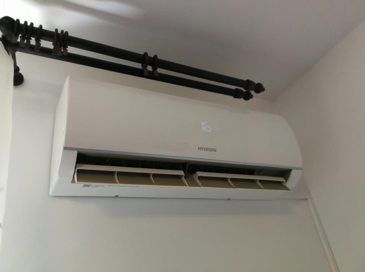 Biała jednostka wewnętrzna klimatyzatora Hyundai zamontowana na ścianie, widoczny wyświetlacz z temperaturą 16 stopni, nad urządzeniem dekoracyjny, ciemny karnisz z metalowymi uchwytami.