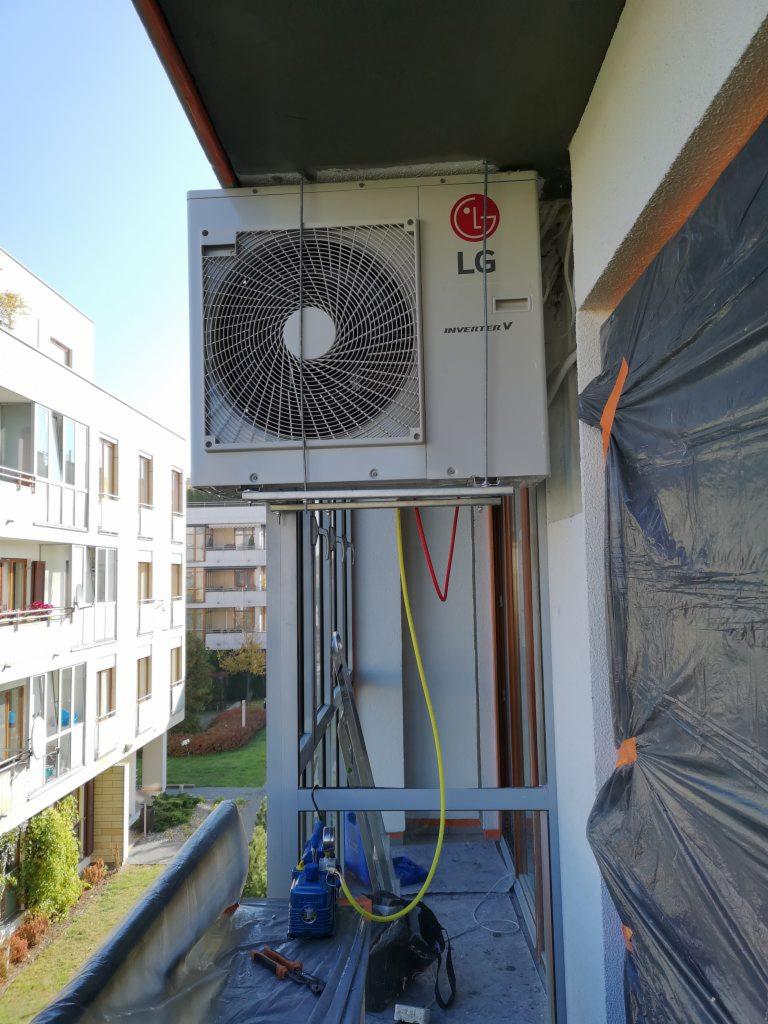 Jednostka zewnętrzna LG Inverter V zamontowana na balkonie bloku mieszkalnego, widoczna drabina, narzędzia i folia ochronna podczas instalacji.
