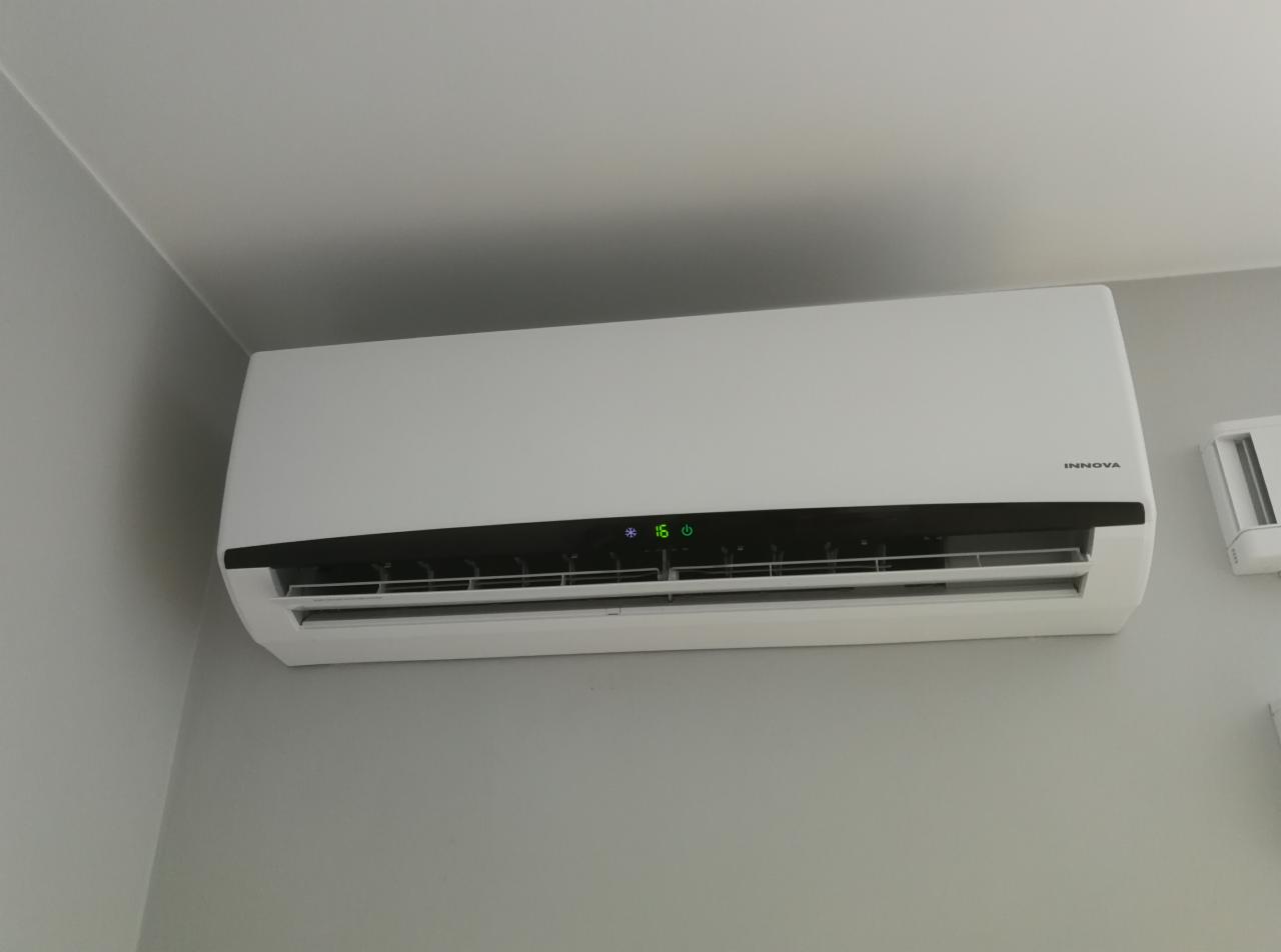 Biały klimatyzator marki Innova zamontowany na szarej ścianie, ustawiony na 16 stopni, widoczny fragment drugiego klimatyzatora po prawej stronie.