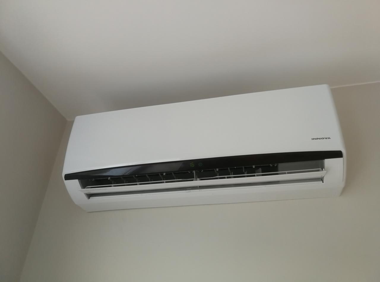 Biała jednostka wewnętrzna klimatyzatora Innova zamontowana na jasnej ścianie, widoczne diody sygnalizacyjne i żaluzje nawiewu.