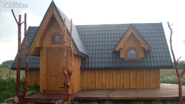 Drewniany domek letniskowy z ciemną dachówką, widoczny z zewnątrz, z dekoracyjnymi elementami z surowego drewna i małym tarasem.