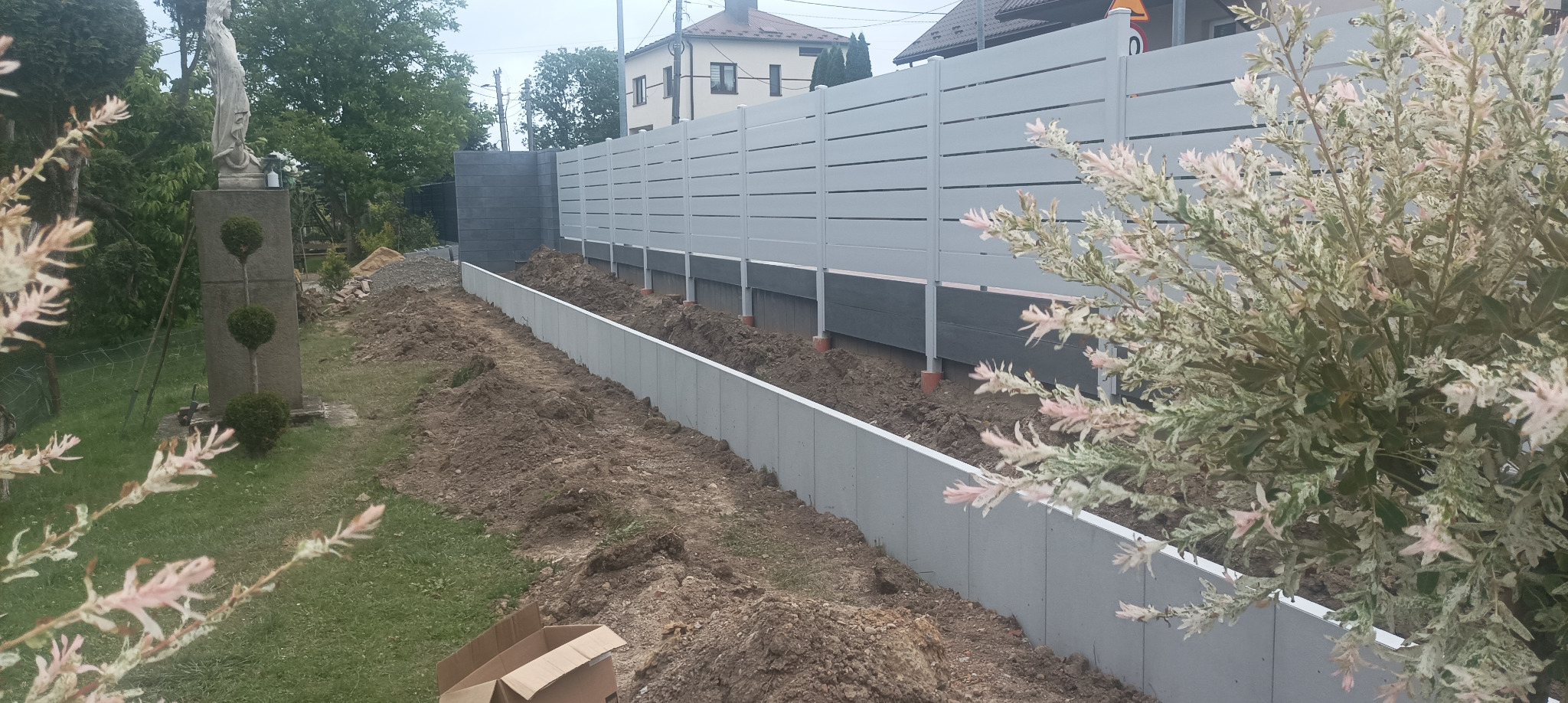 Nowoczesne ogrodzenie panelowe w kolorze szarym, z betonową podmurówką, w trakcie montażu. Widoczne elementy konstrukcyjne i przygotowany teren.