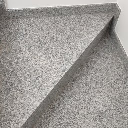 Rafał Witkowski - Granitowe schody wykończone z precyzją, widoczne z góry, z fragmentem buta w prawym dolnym rogu, kontrastujące z białą ścianą w tle.