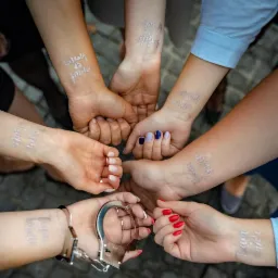 Grupowe zdjęcie dłoni z tymczasowymi tatuażami 'Team Bride' i 'Bride' oraz kajdankami na jednym nadgarstku, symbolizujące wieczór panieński.